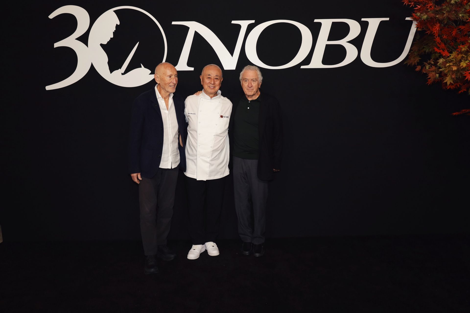 Nobu 30th anniversary event: Three men posing in front of a logo on a black background.