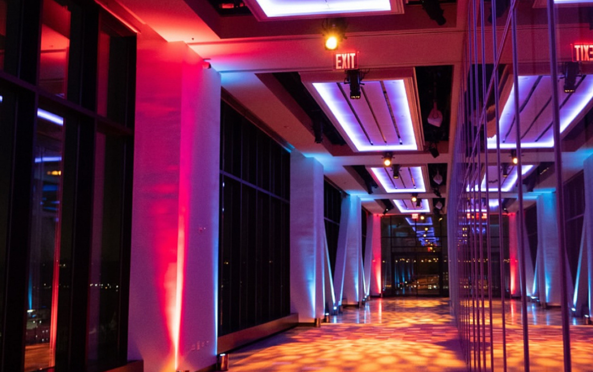 Hallway lit with red and blue lights, tall windows, mirrored structure, and exit signs.