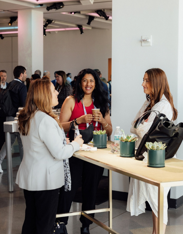 Three people talking near a table with plants in a brightly lit room.
