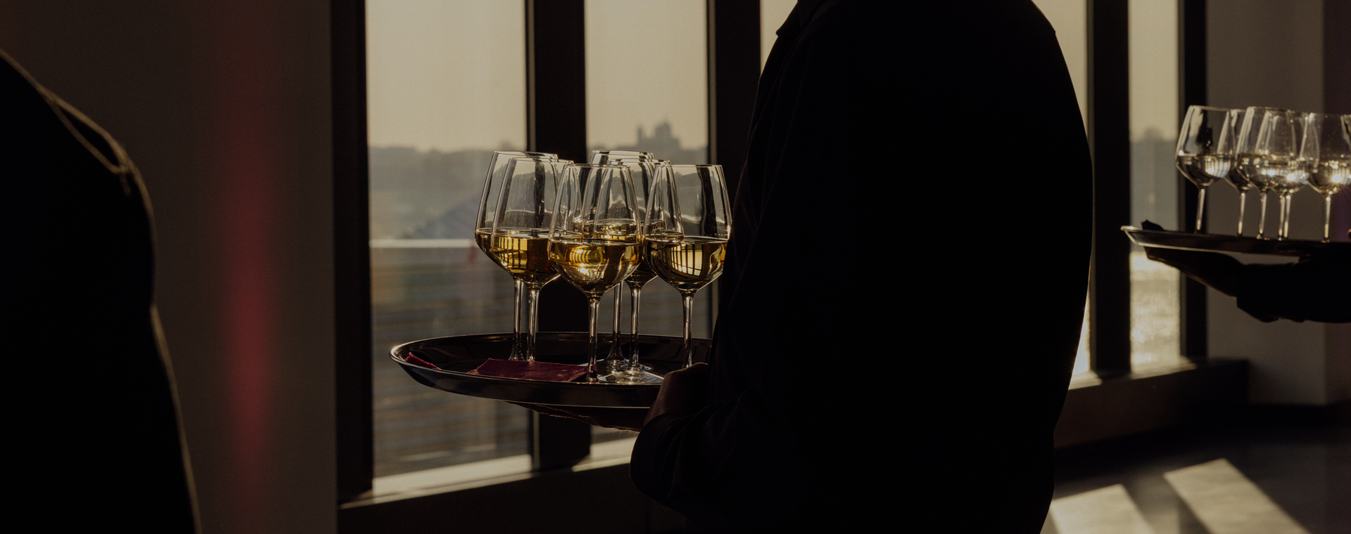 Silhouetted person beside tables of champagne flutes by a sunlit window
