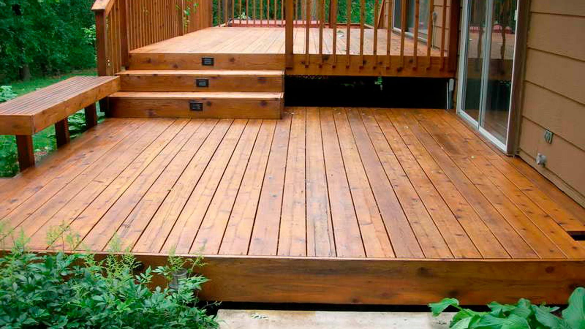 A multi-level stained wood deck featuring a bench, stairs with integrated lighting, and a sliding glass door entrance.