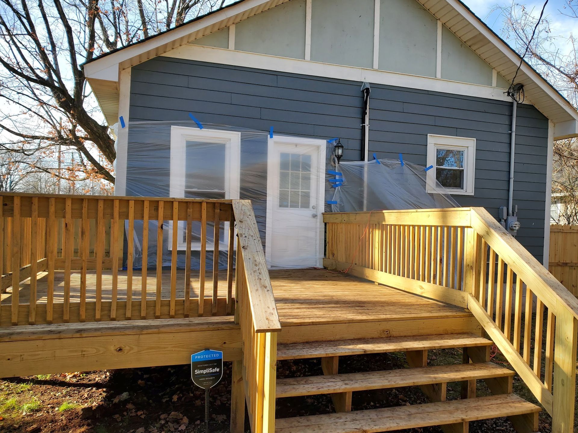 A house exterior under renovation with blue siding, a new wooden deck and stairs, and a white door and window frames.