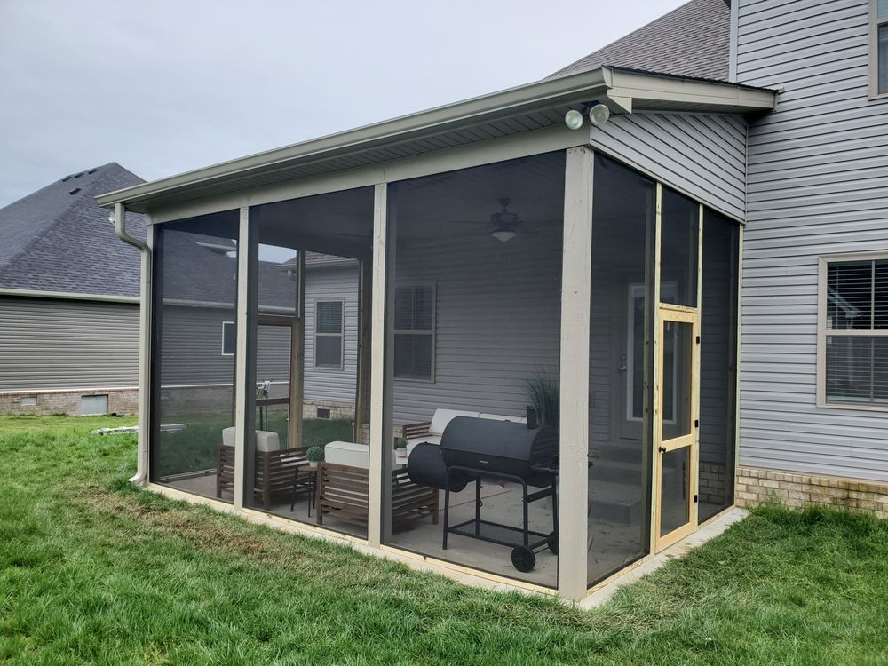 A beige-trimmed screened-in porch with a charcoal grill and outdoor furniture, attached to a gray house with vinyl siding.