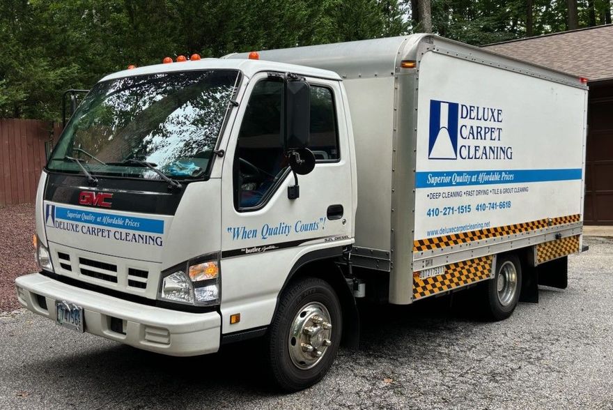 A white GMC box truck parked on gravel, branded with the 
