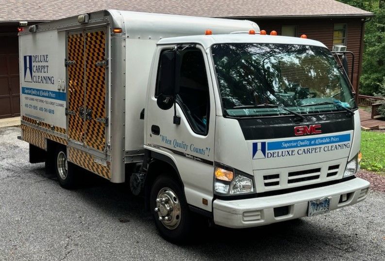 A white Deluxe Carpet Cleaning box truck parked in a residential driveway.