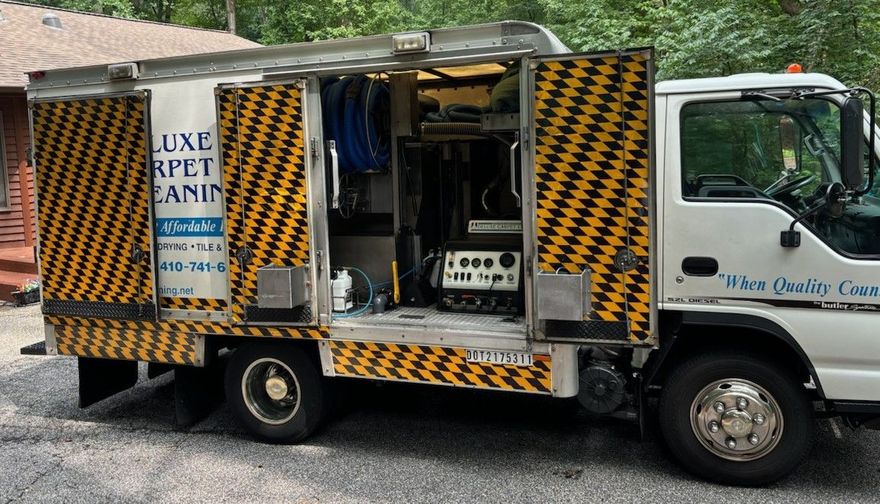 White utility truck with yellow and black chevron patterned side panels, identified as a carpet cleaning vehicle.