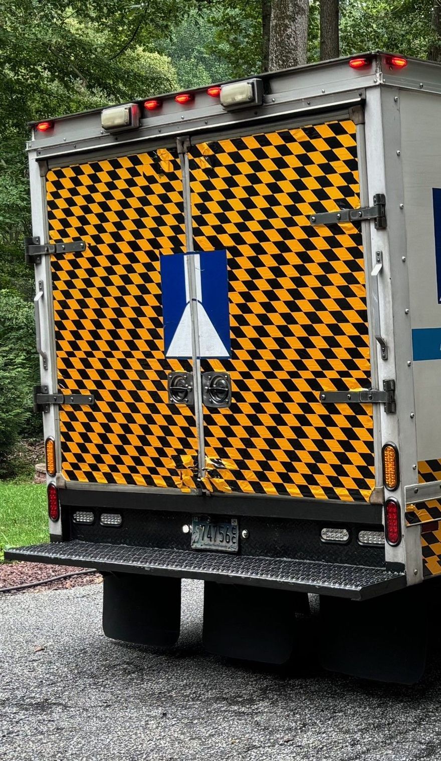Rear view of a box truck featuring a yellow and black checkered pattern and a central blue and white emblem.
