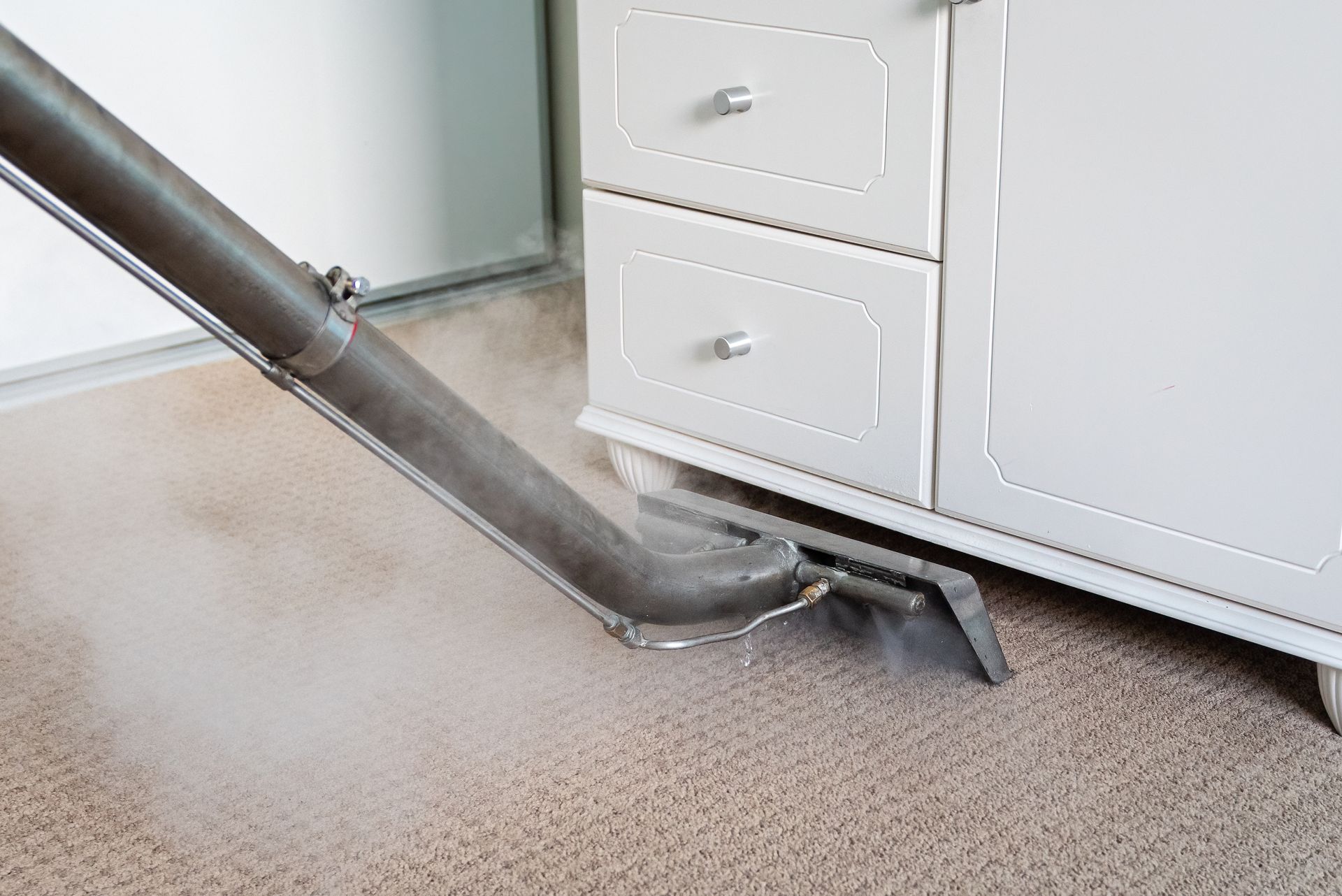 Vacuum cleaner hose under a white cabinet on beige carpet