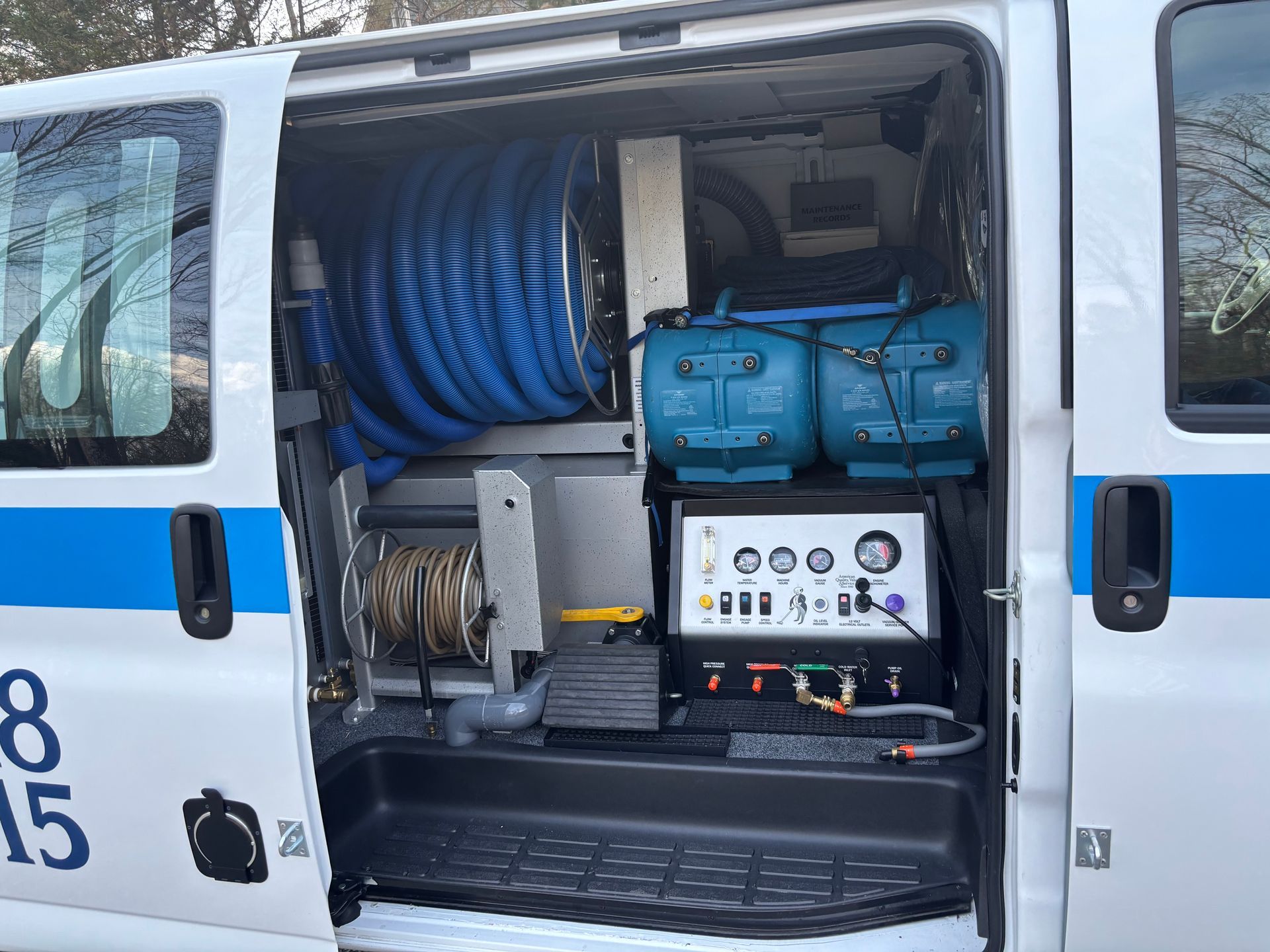 The side door of a white utility van is open, revealing a carpet cleaning machine with blue hoses and control gauges. The side door of a white utility van is open, revealing a carpet cleaning machine with blue hoses and control gauges.