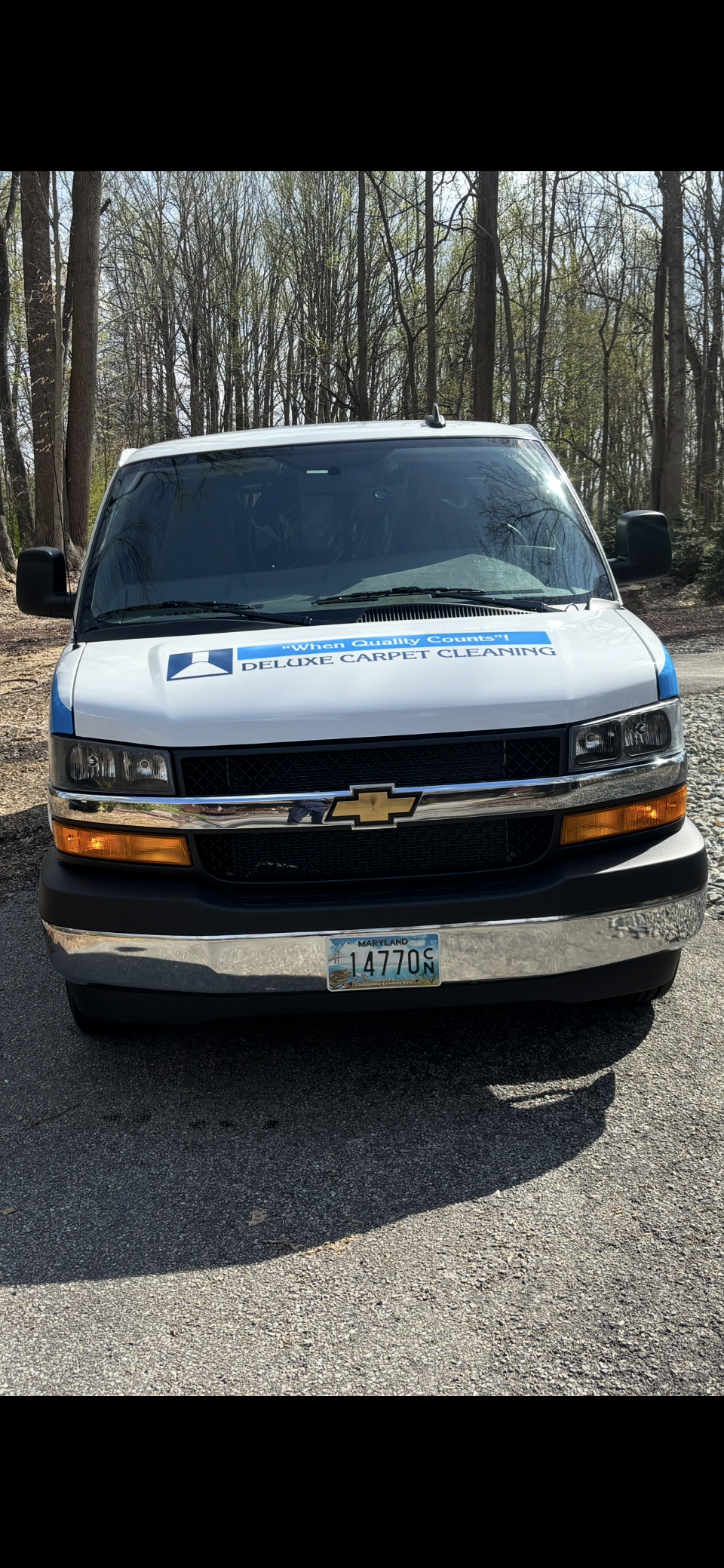 A white Chevrolet work van parked on a gravel path in front of trees.