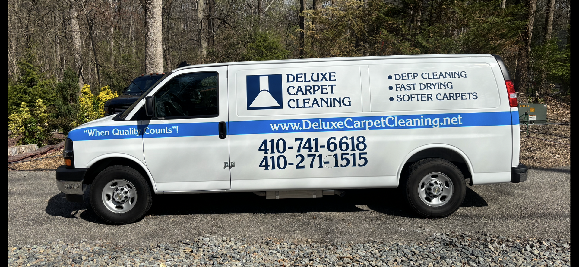 White service van for Deluxe Carpet Cleaning parked outdoors, displaying contact info and website on its side.