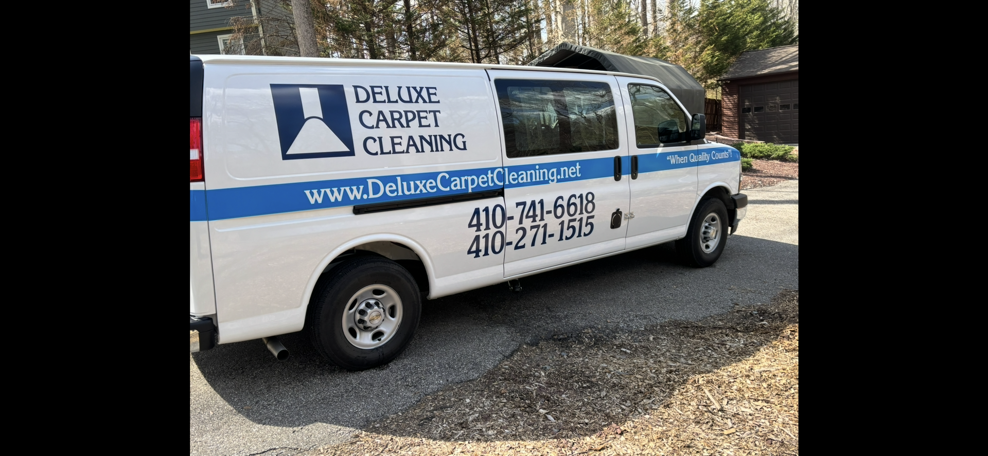 White Deluxe Carpet Cleaning work van parked on a gravel driveway with blue branding, website, and phone numbers.
