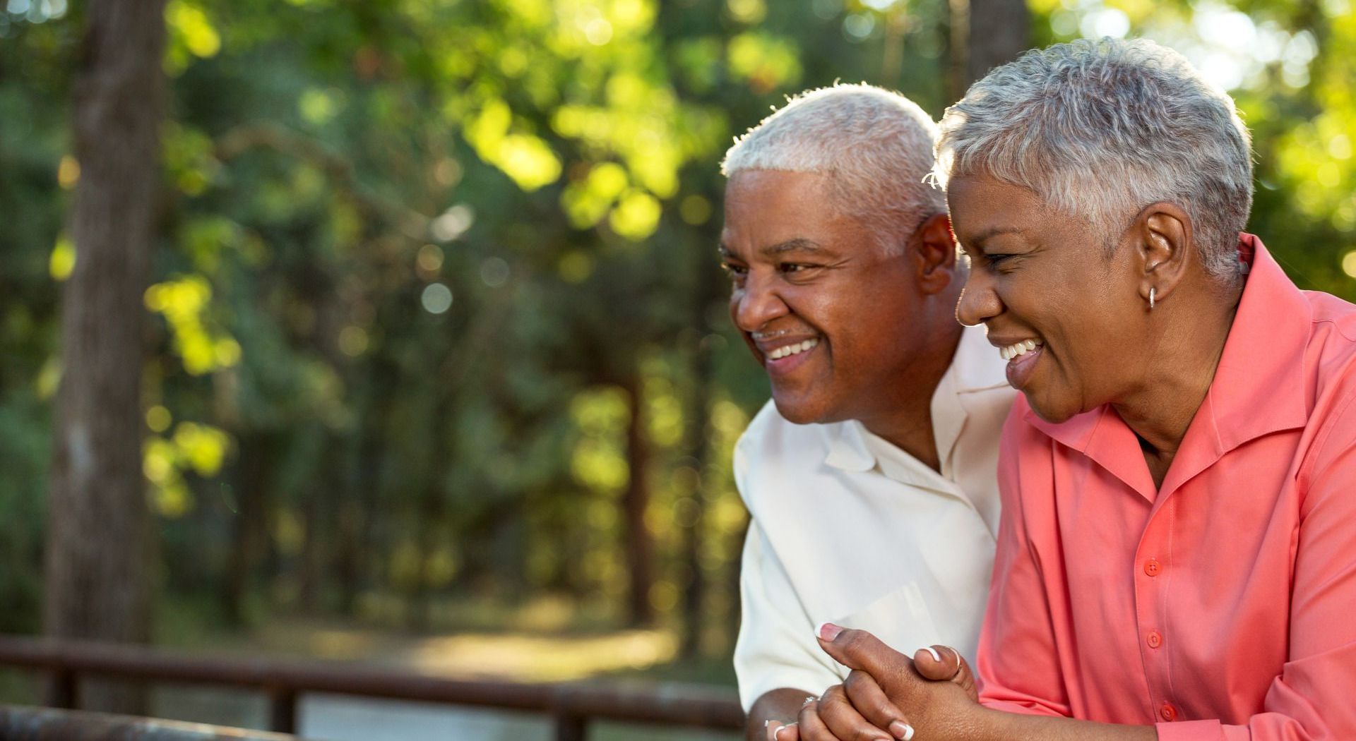 A man and a woman are sitting next to each other in a park holding hands and smiling.