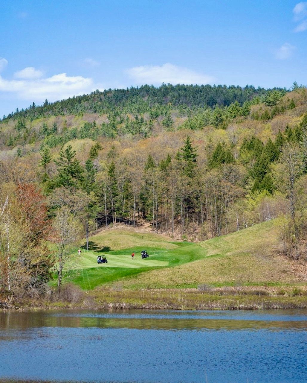 A golf course with a lake in the foreground and mountains in the background.