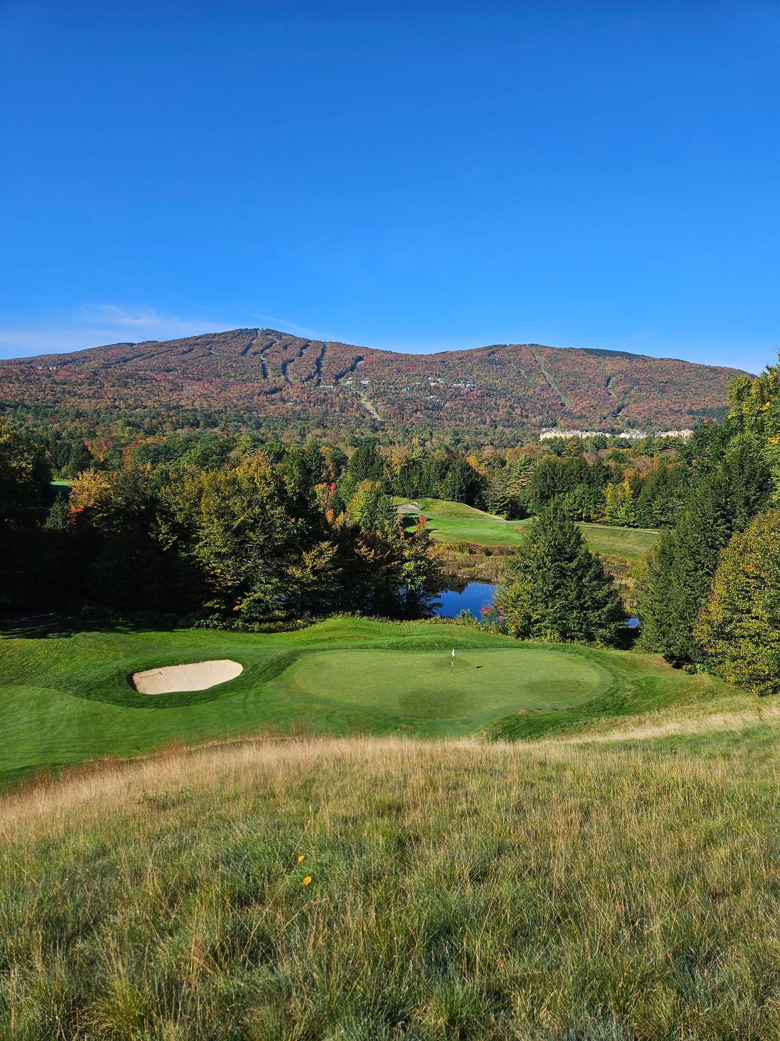 A view of a golf course with mountains in the background on a sunny day.