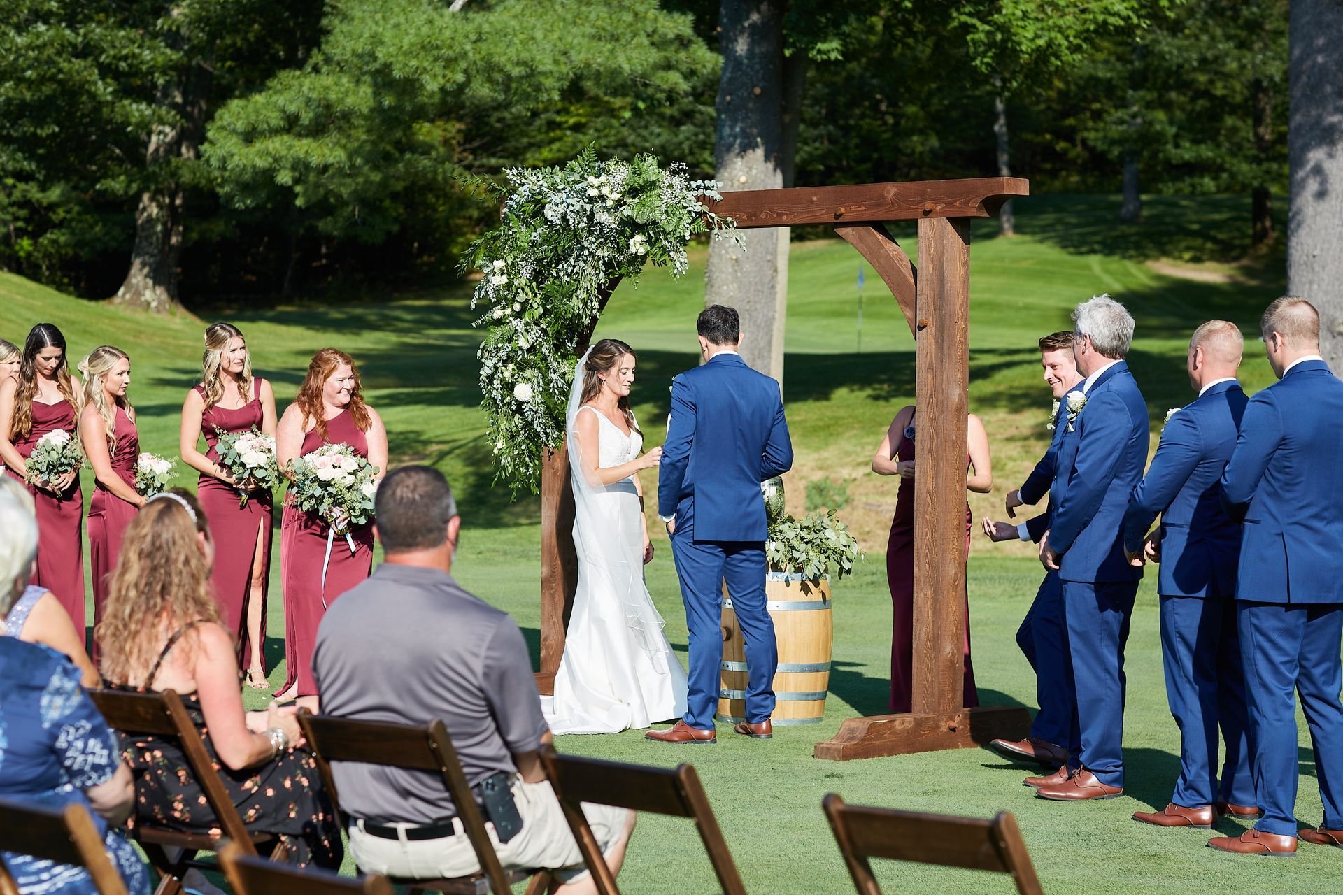 A bride and groom are standing under a wooden arch at their wedding ceremony.