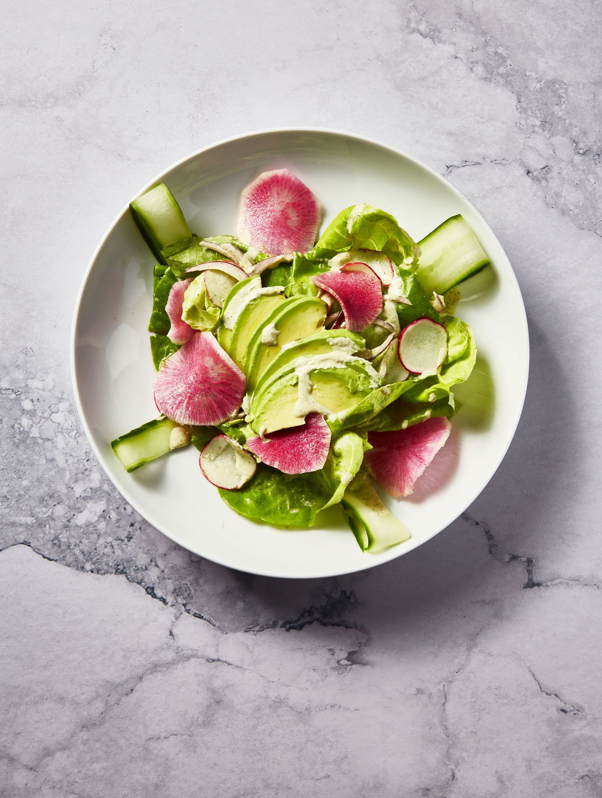 A white plate topped with a salad of avocado , radishes , cucumbers and lettuce.