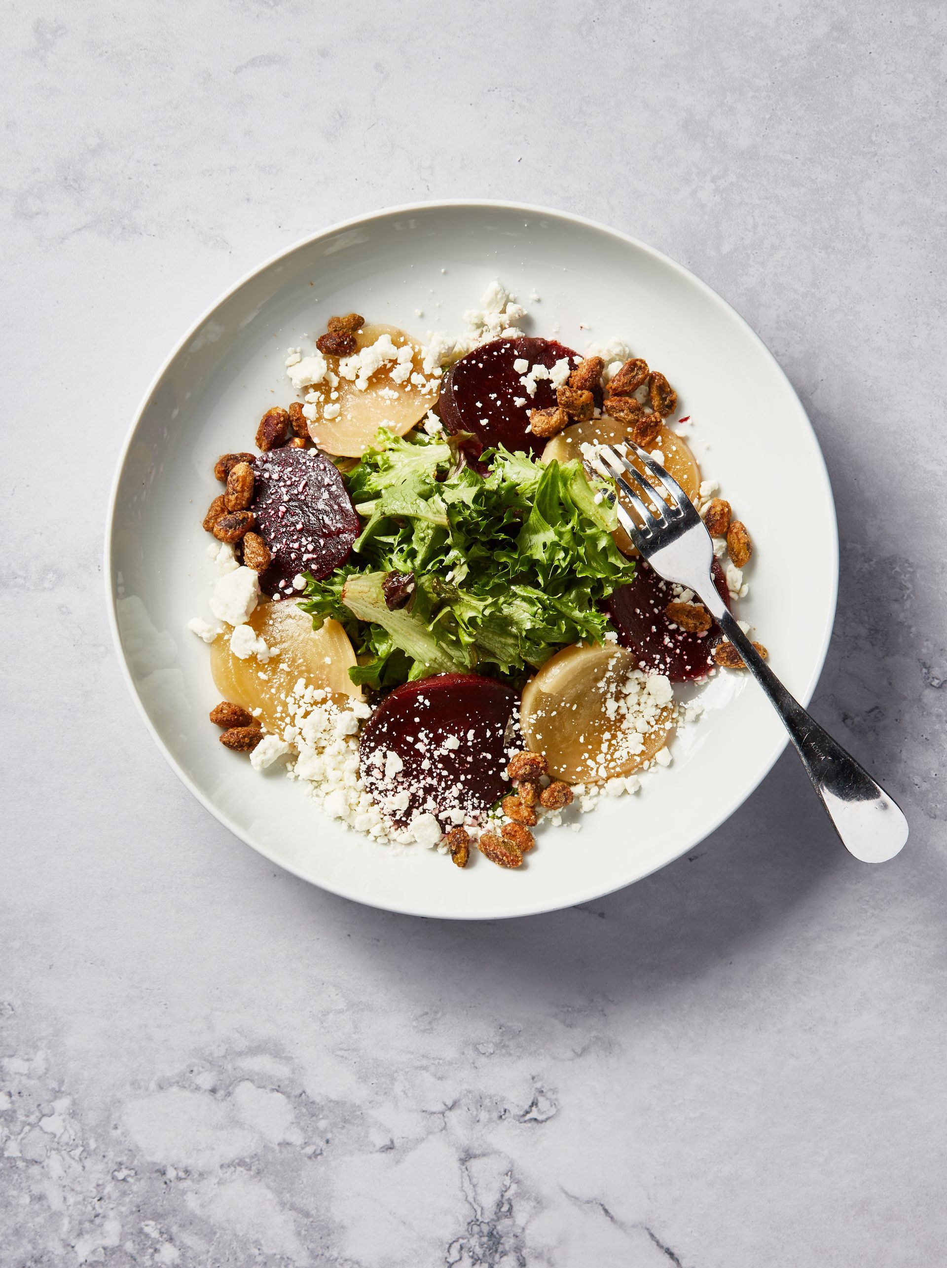 A white plate topped with a salad and a fork on a table.