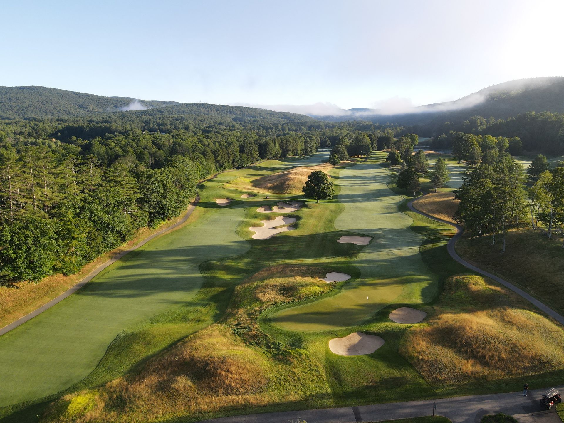 An aerial view of a golf course surrounded by trees and mountains.