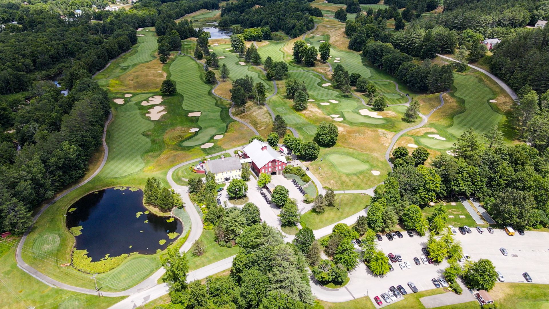 An aerial view of a golf course surrounded by trees and a pond.
