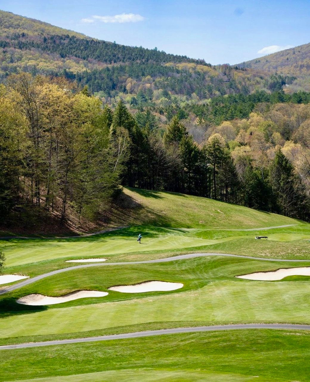 A golf course surrounded by mountains and trees on a sunny day.