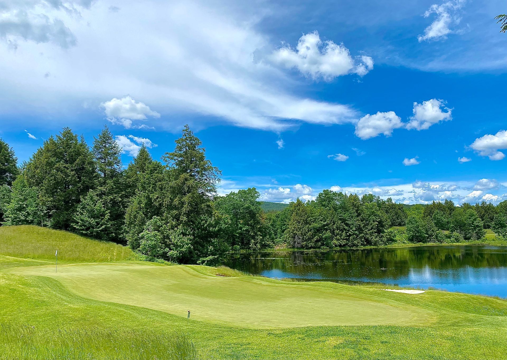 A golf course with a lake in the background and trees in the foreground.
