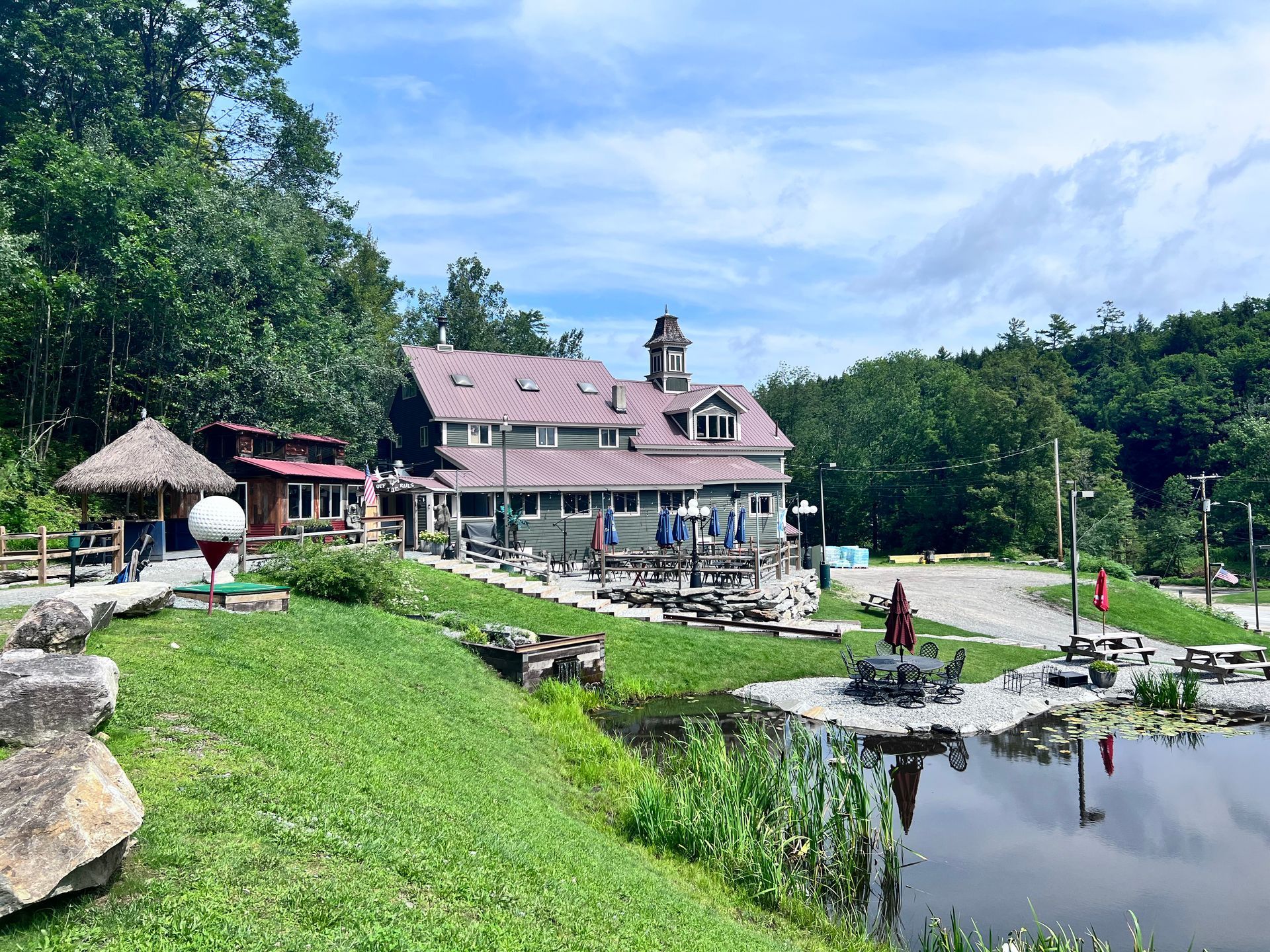 A large house is sitting on top of a lush green hill next to a pond.