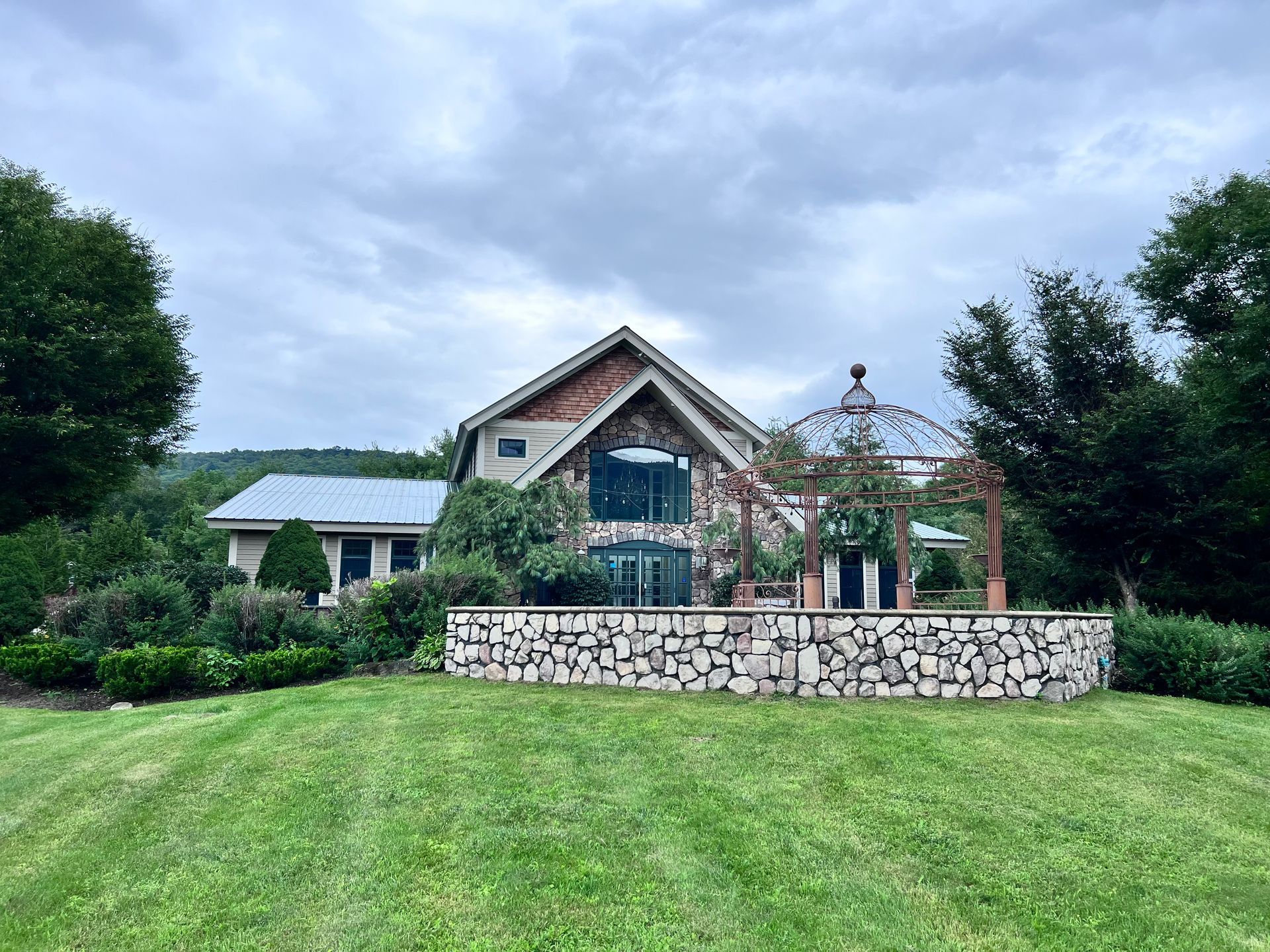 A large house with a gazebo in front of it is surrounded by trees and grass.