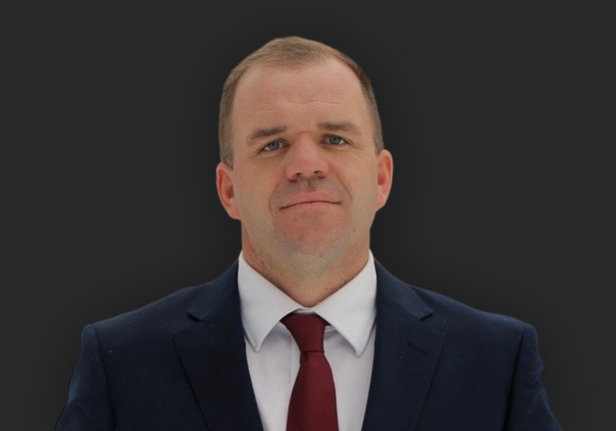 A man in a plaid shirt is smiling with his arms crossed.