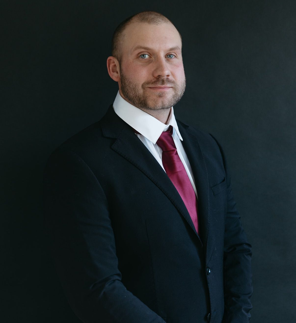 A man in a plaid shirt is smiling with his arms crossed.