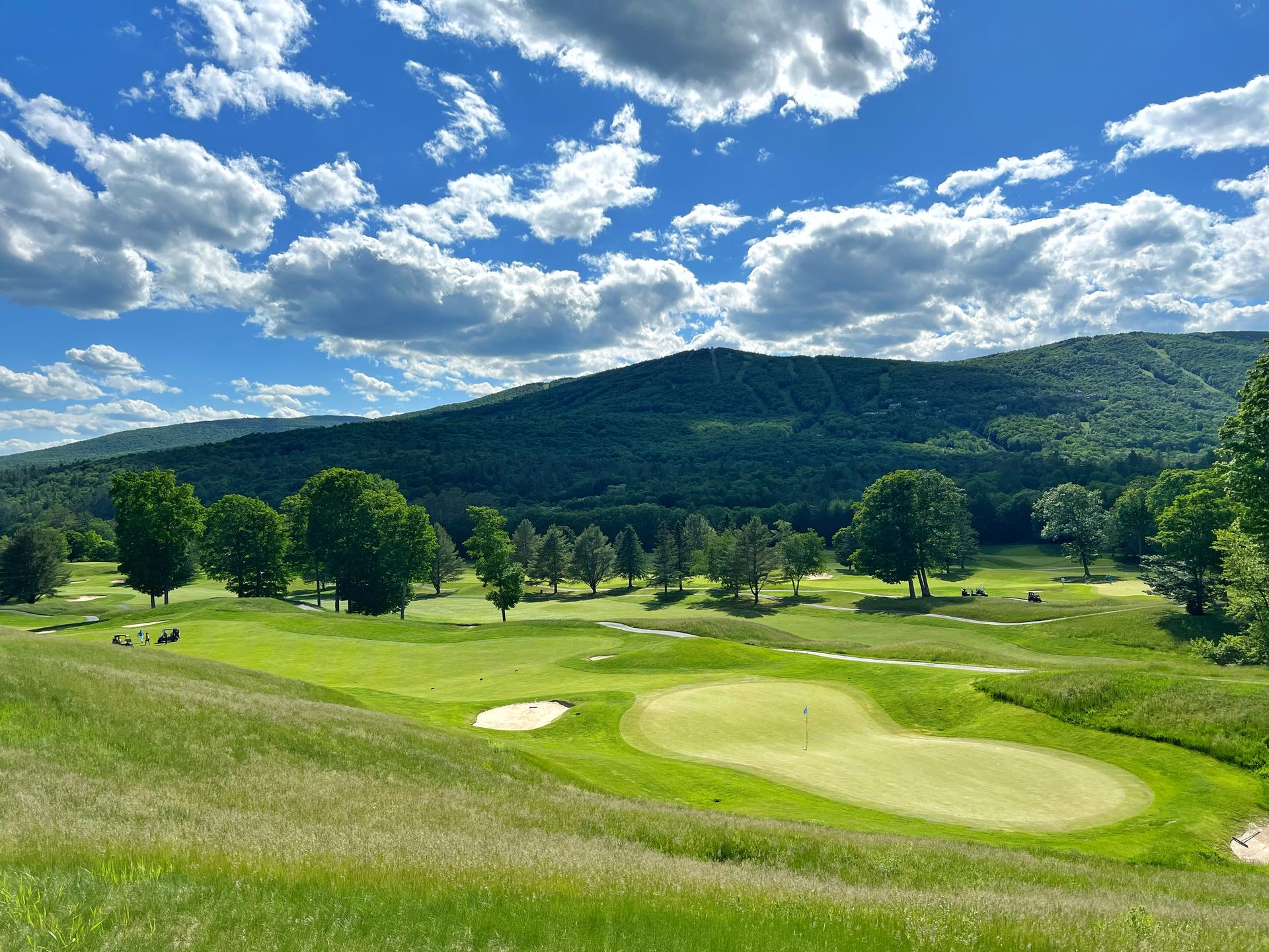 A view of a golf course with mountains in the background on a sunny day.