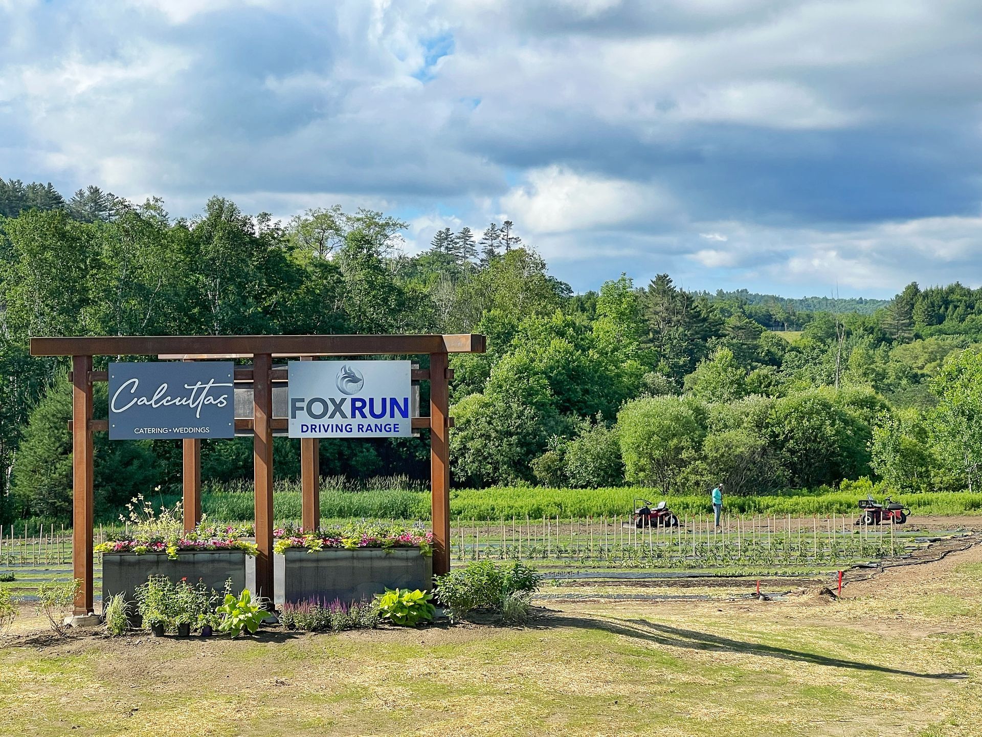 A wooden sign in the middle of a field with trees in the background.