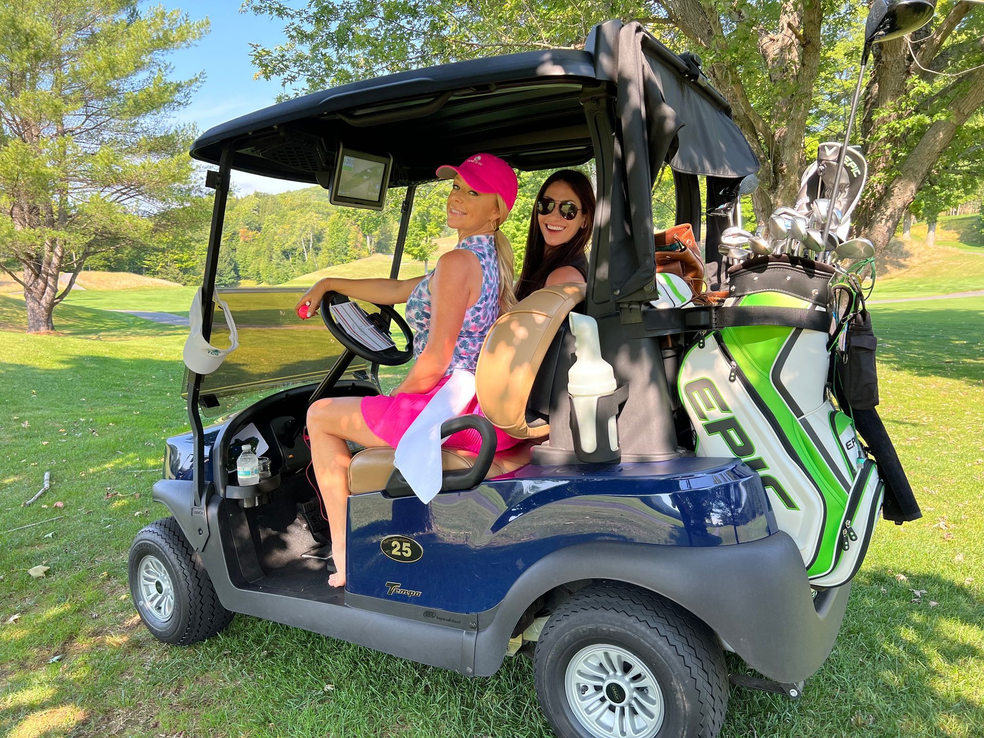 Two women are sitting in a golf cart on a golf course.