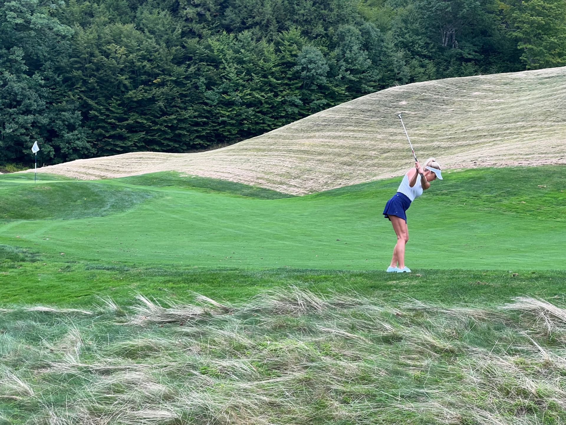 A woman is swinging a golf club on a golf course.