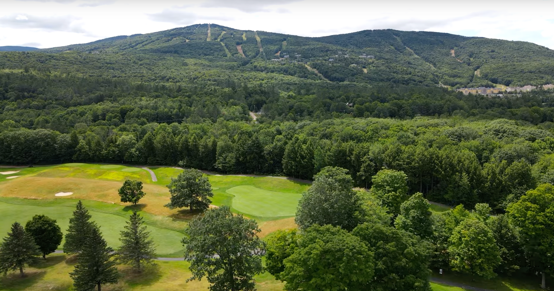 An aerial view of a golf course surrounded by trees and mountains.