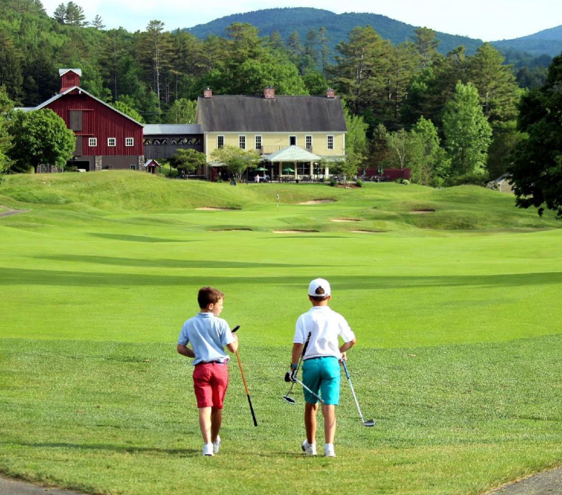 Two people standing on a golf course with a red barn in the background