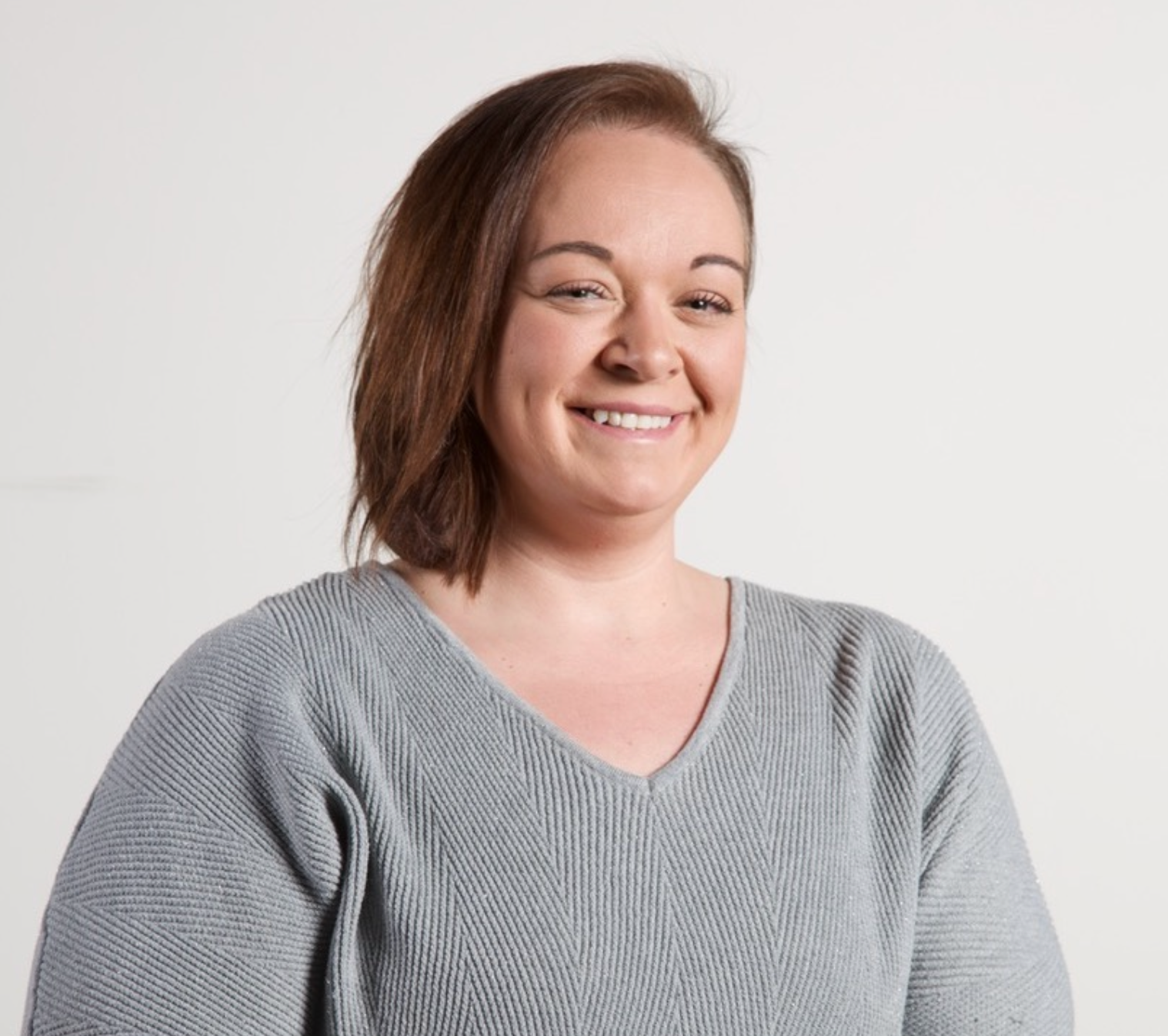 A woman wearing a grey sweater is smiling for the camera