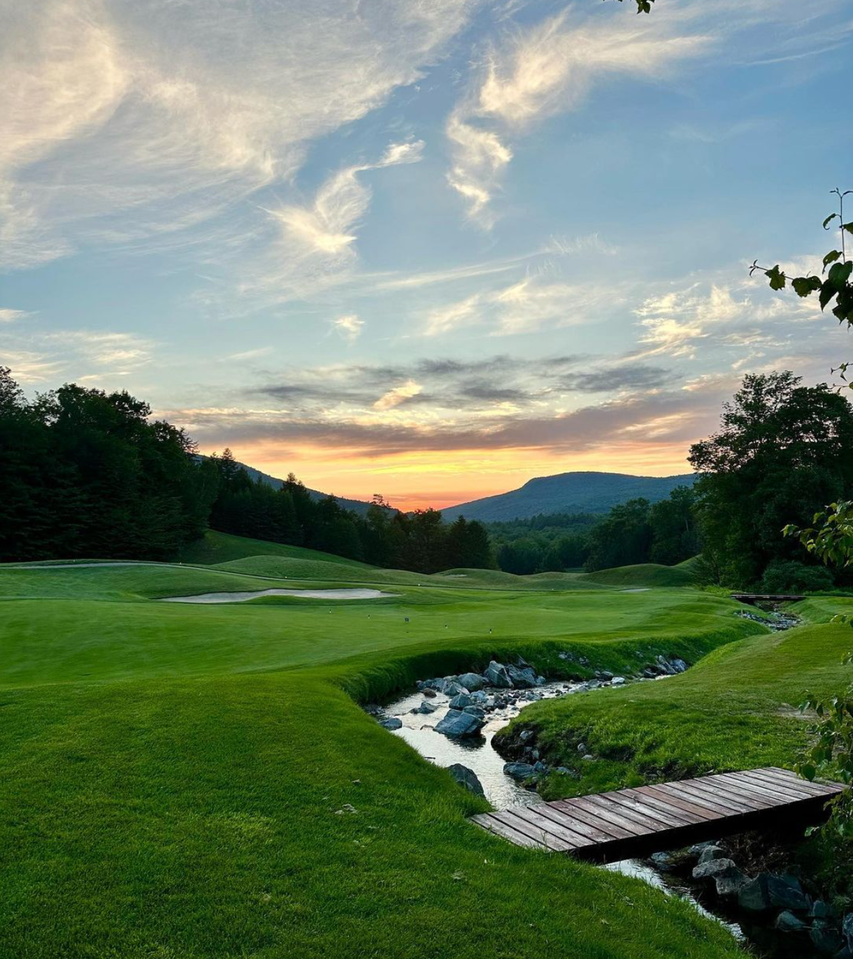 A bridge over a stream on a golf course at sunset