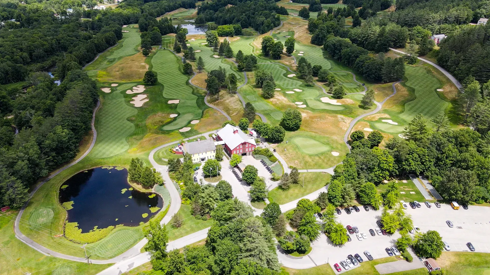 An aerial view of a golf course surrounded by trees and a pond.