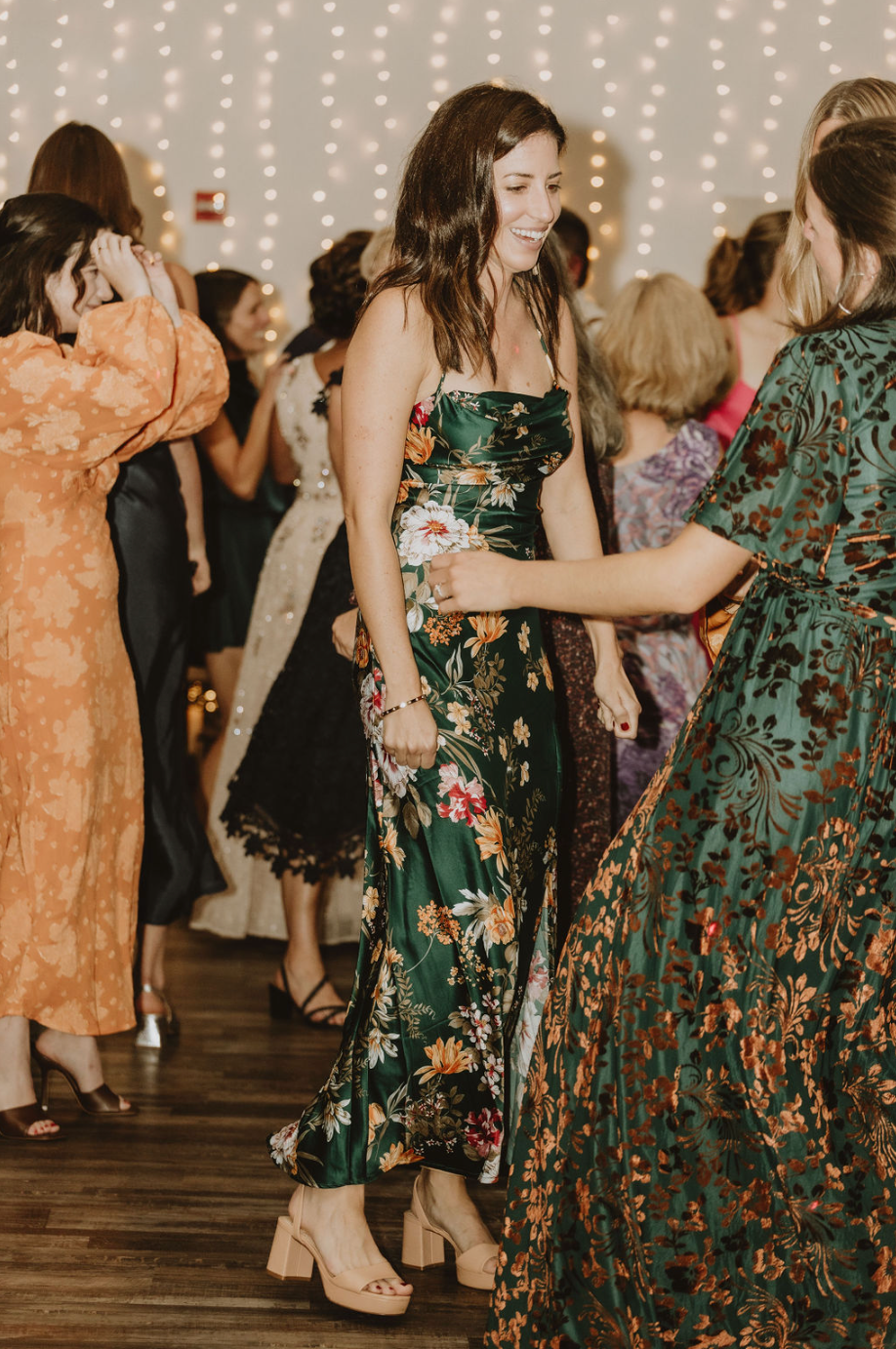 A woman in a green dress is dancing with a group of women at a wedding reception.