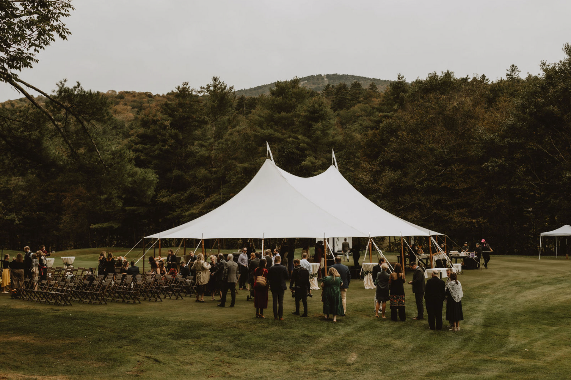 A group of people are standing in a field in front of a large white tent.