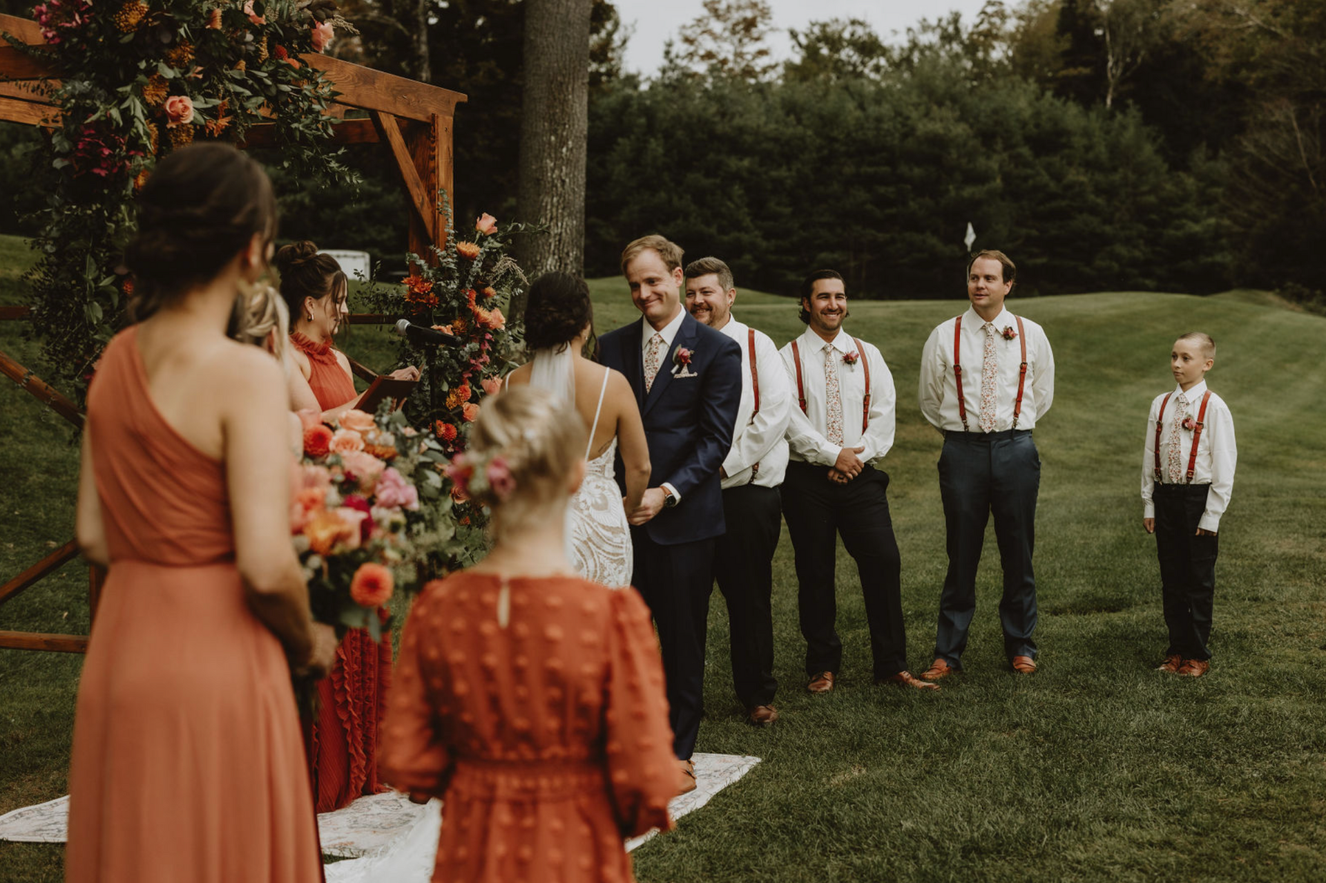 A bride and groom are getting married in a field with their wedding party.