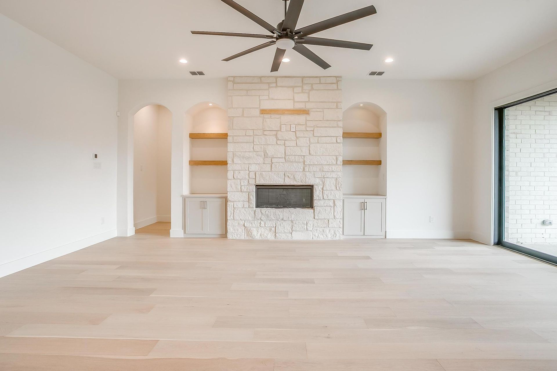An empty living room with a fireplace and a ceiling fan.