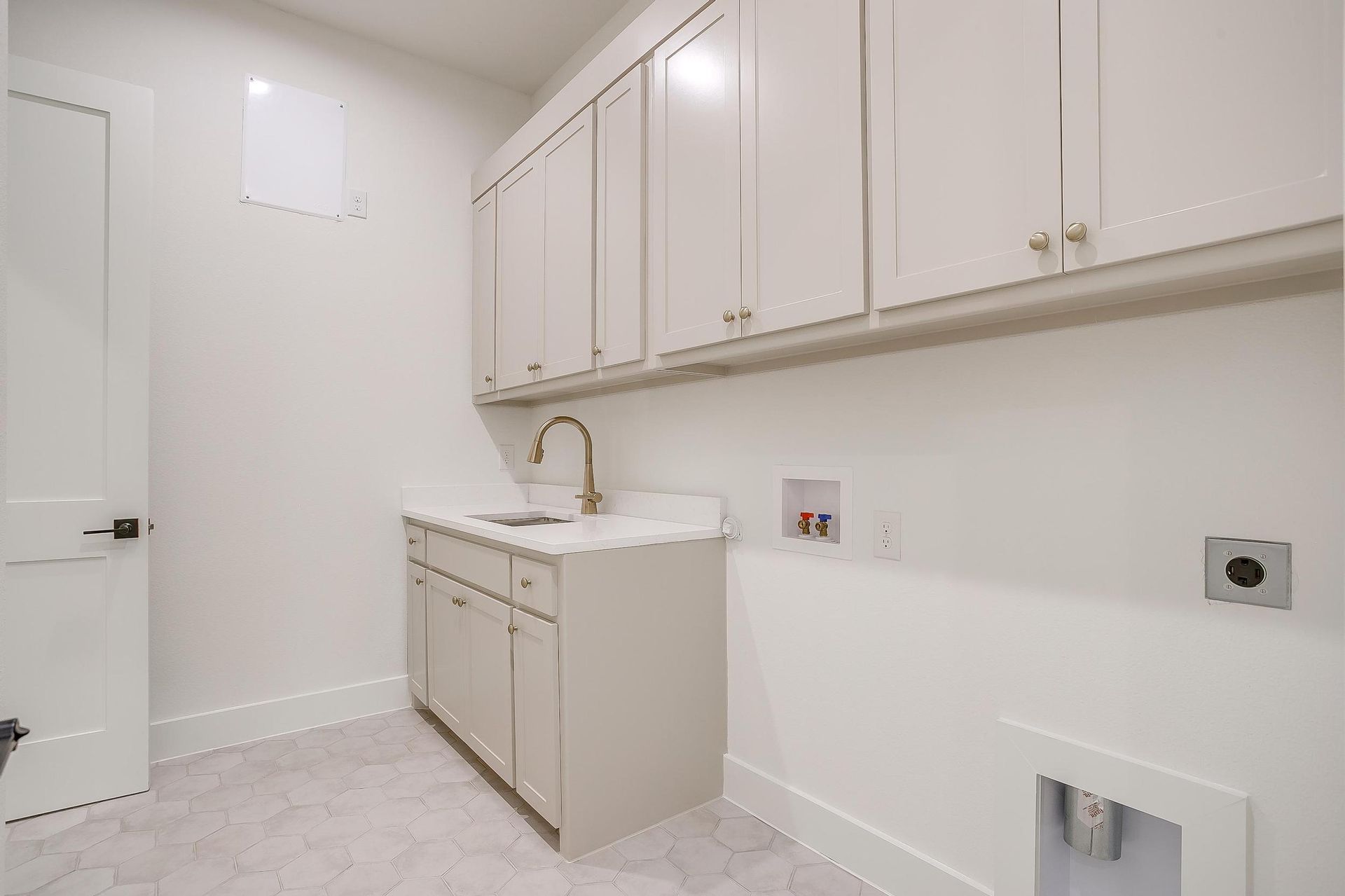 A laundry room with white cabinets and a sink.