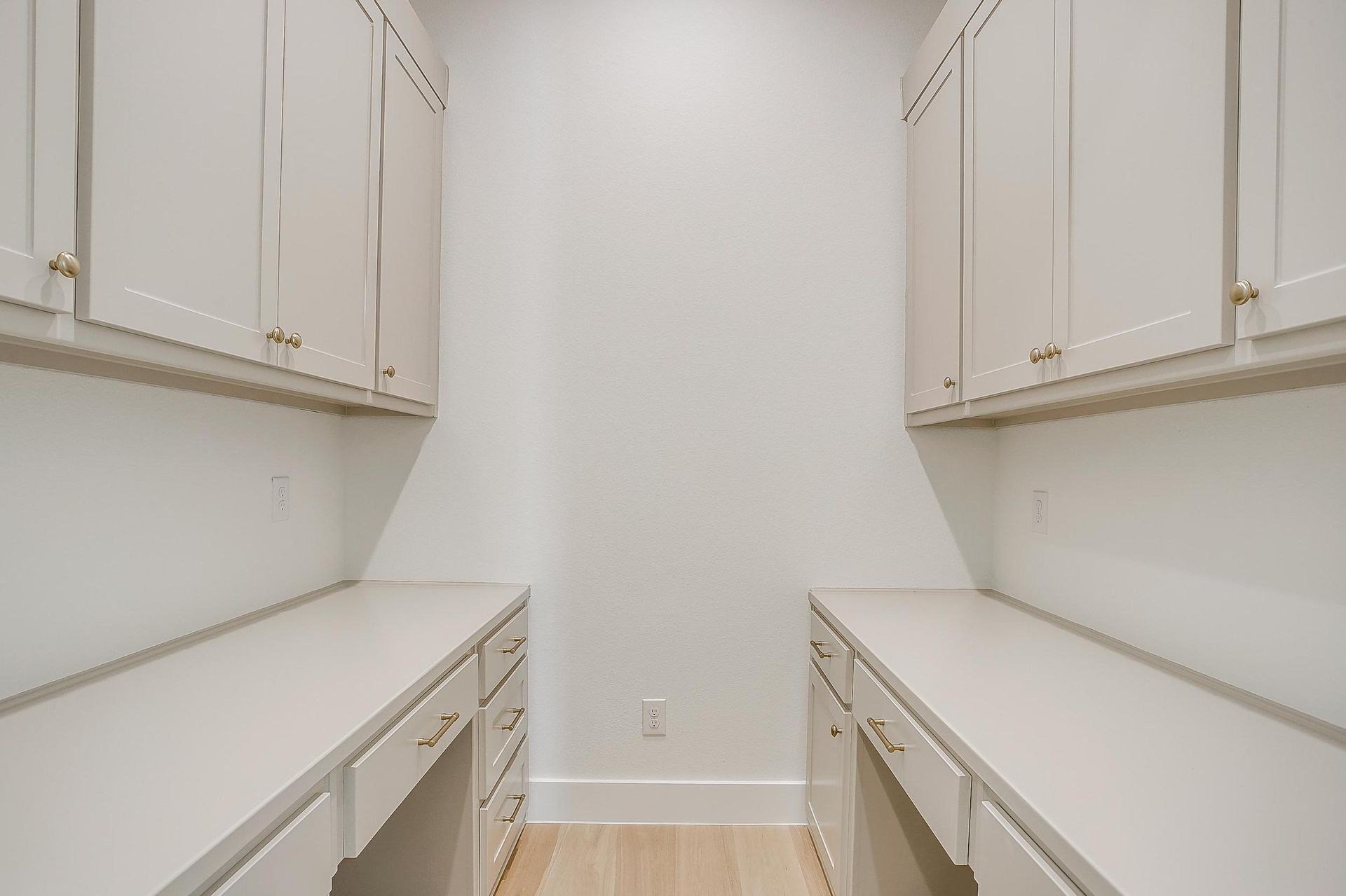 There are two desks in this room with white cabinets.