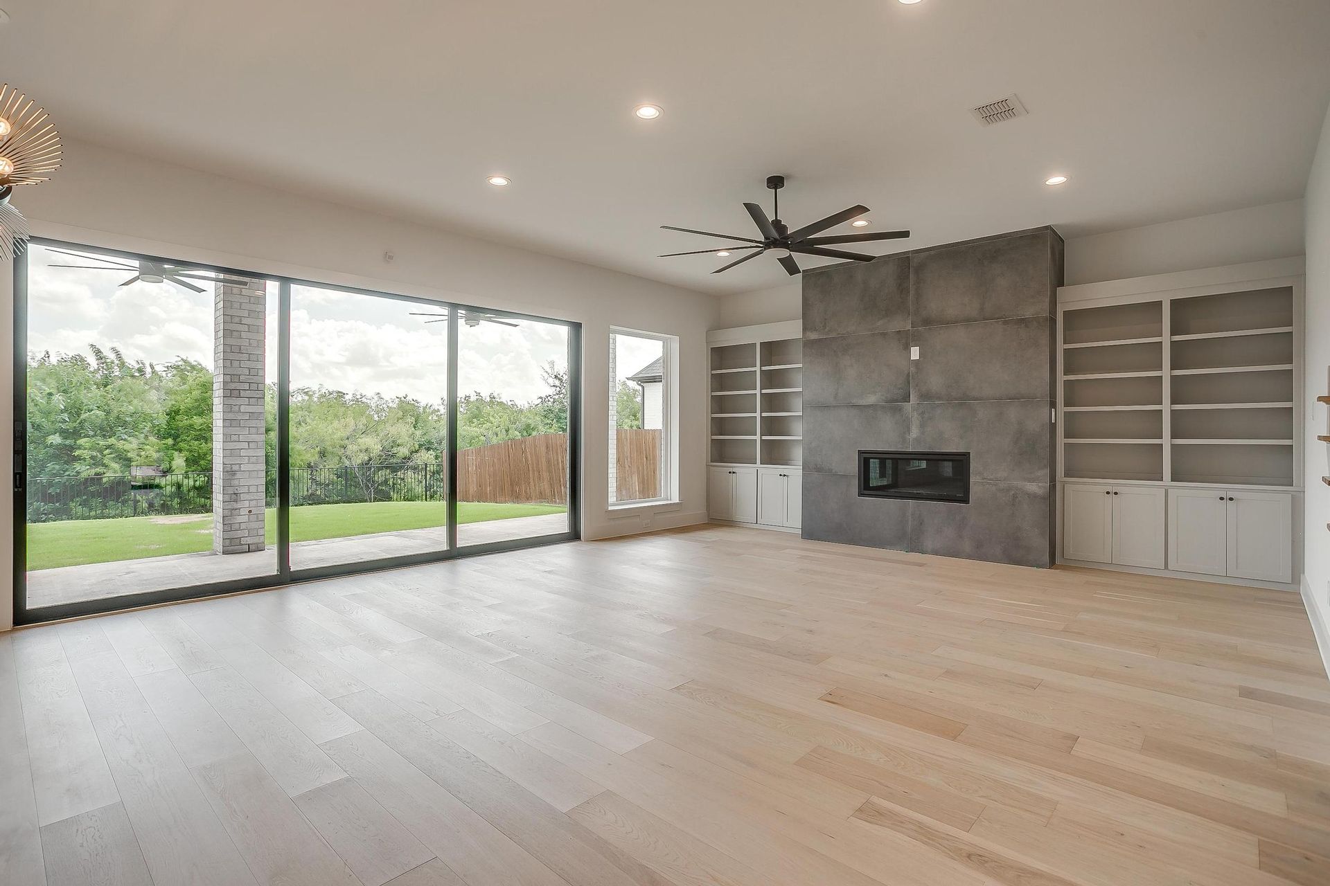 An empty living room with hardwood floors , sliding glass doors , a fireplace and a ceiling fan.