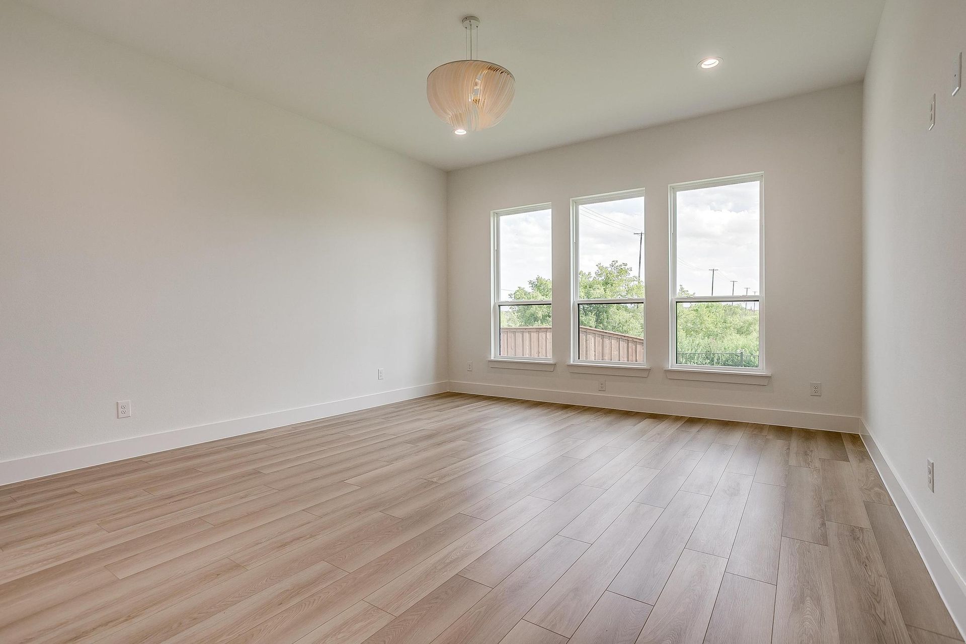 A large empty room with hardwood floors and three windows.