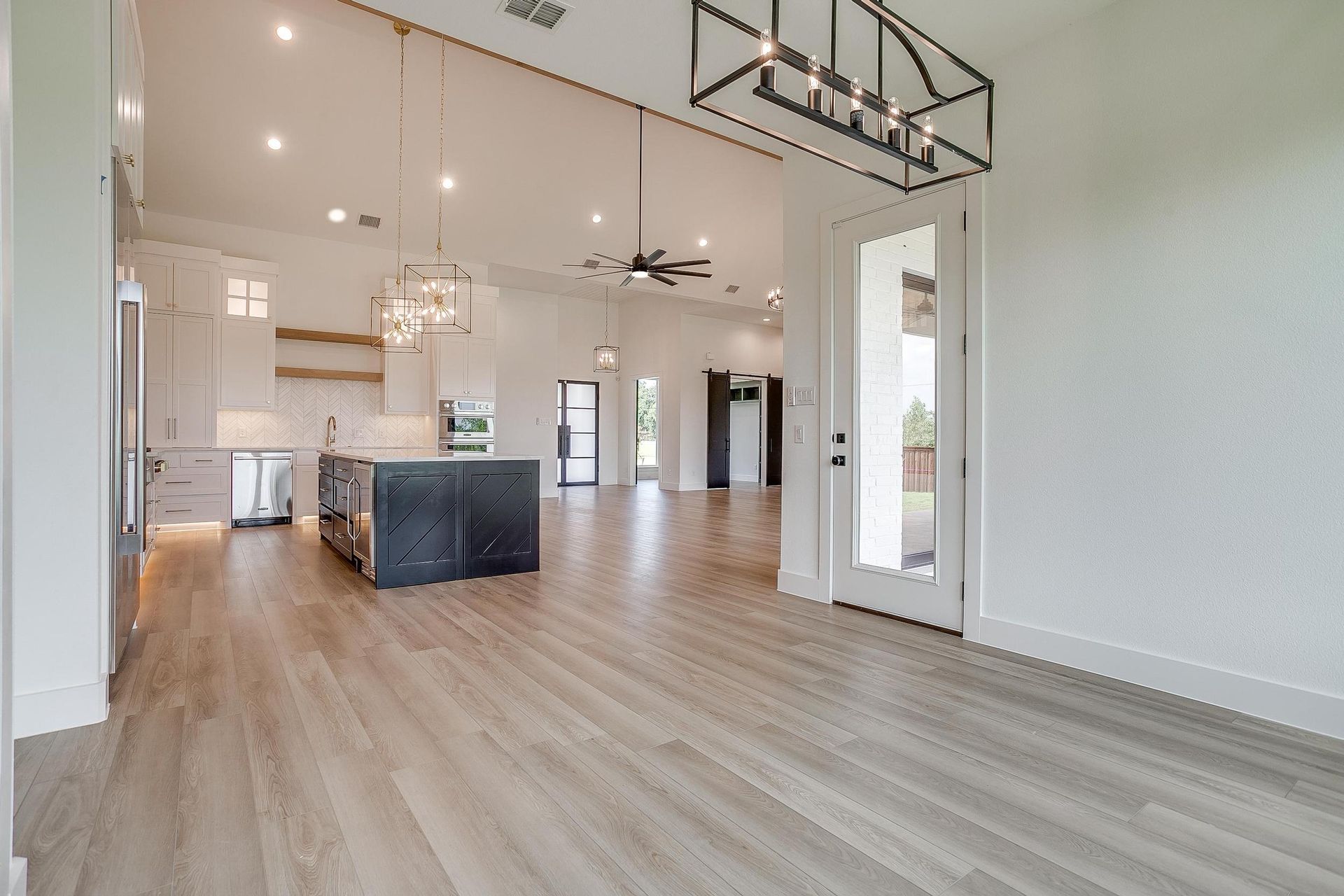 A large empty room with hardwood floors and a kitchen in the background.