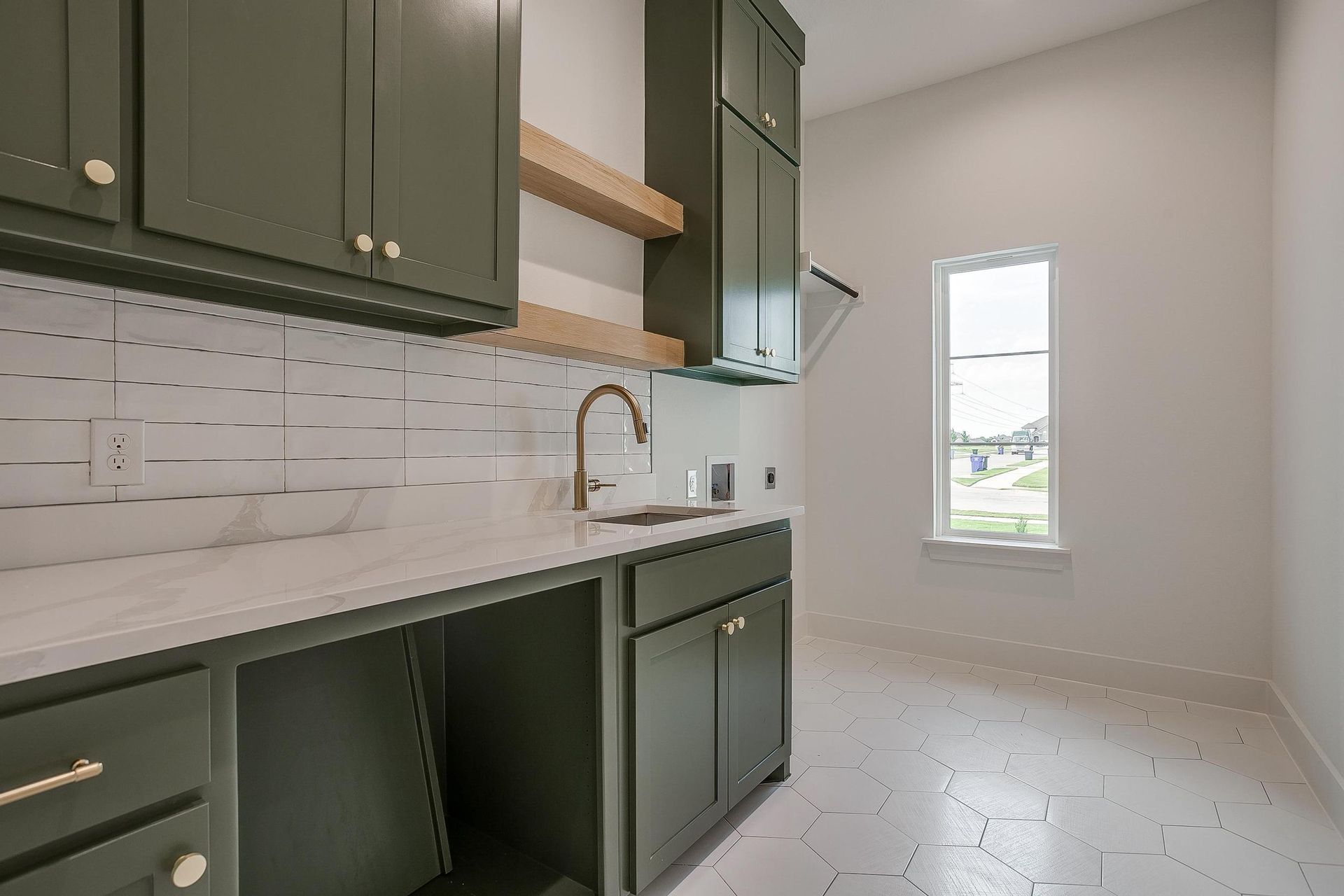 A kitchen with green cabinets , white counter tops , a sink and a window.