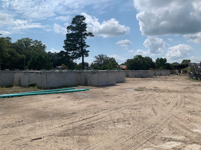 Empty dirt lot with concrete walls, trees, and a cloudy sky